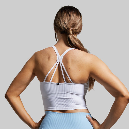Woman wearing a white sports bra and blue shorts on a gray background