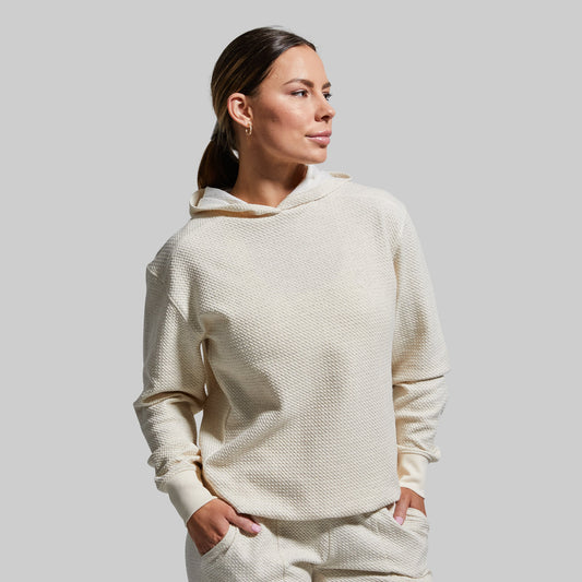 A woman wearing a beige hooded hoodie with a waffle-textured material.