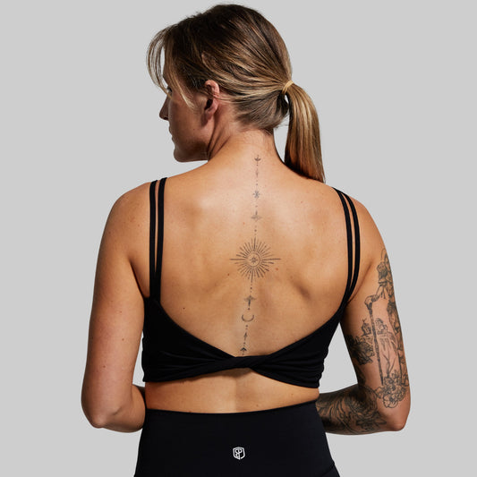 Woman wearing a black sports bra with visible tattoos on a plain background